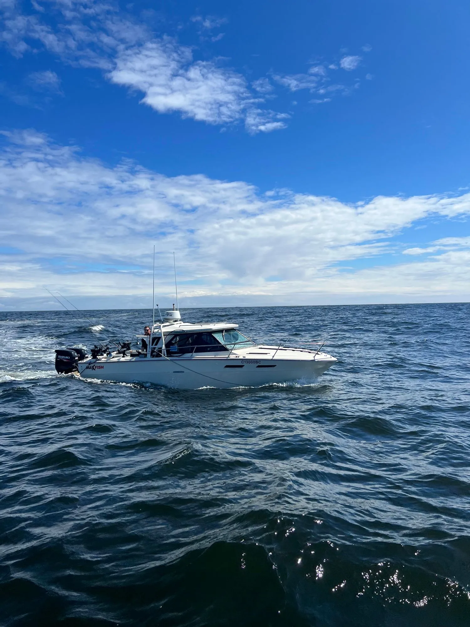 A boat sails on a calm ocean under a blue sky with scattered clouds.