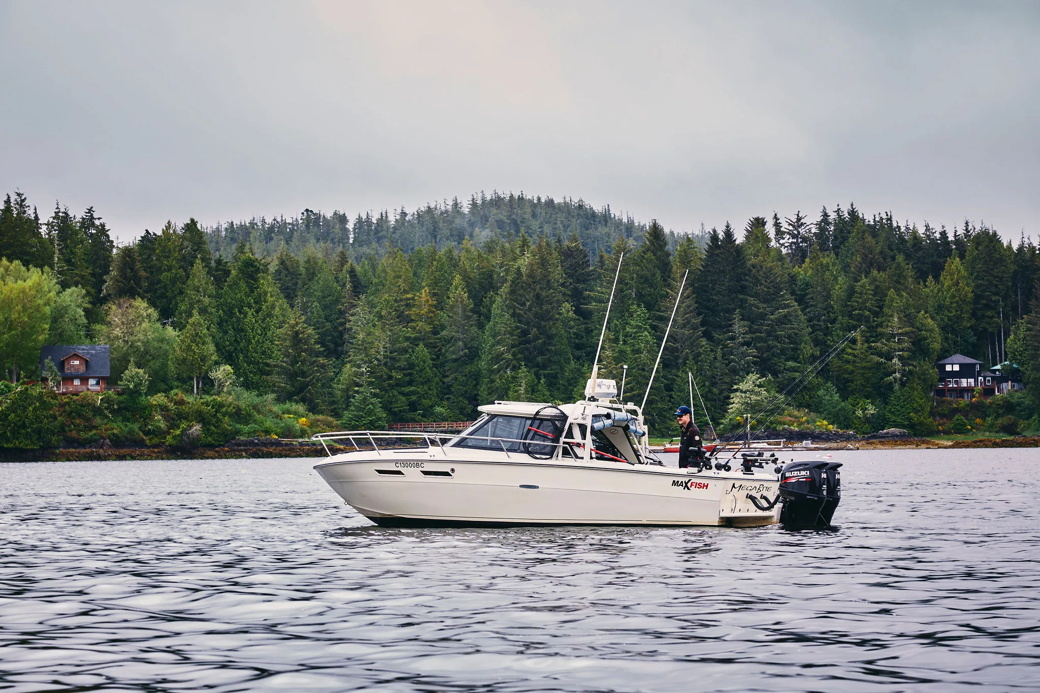 Boat on a lake with forested hillside in the background; overcast sky, calm water.