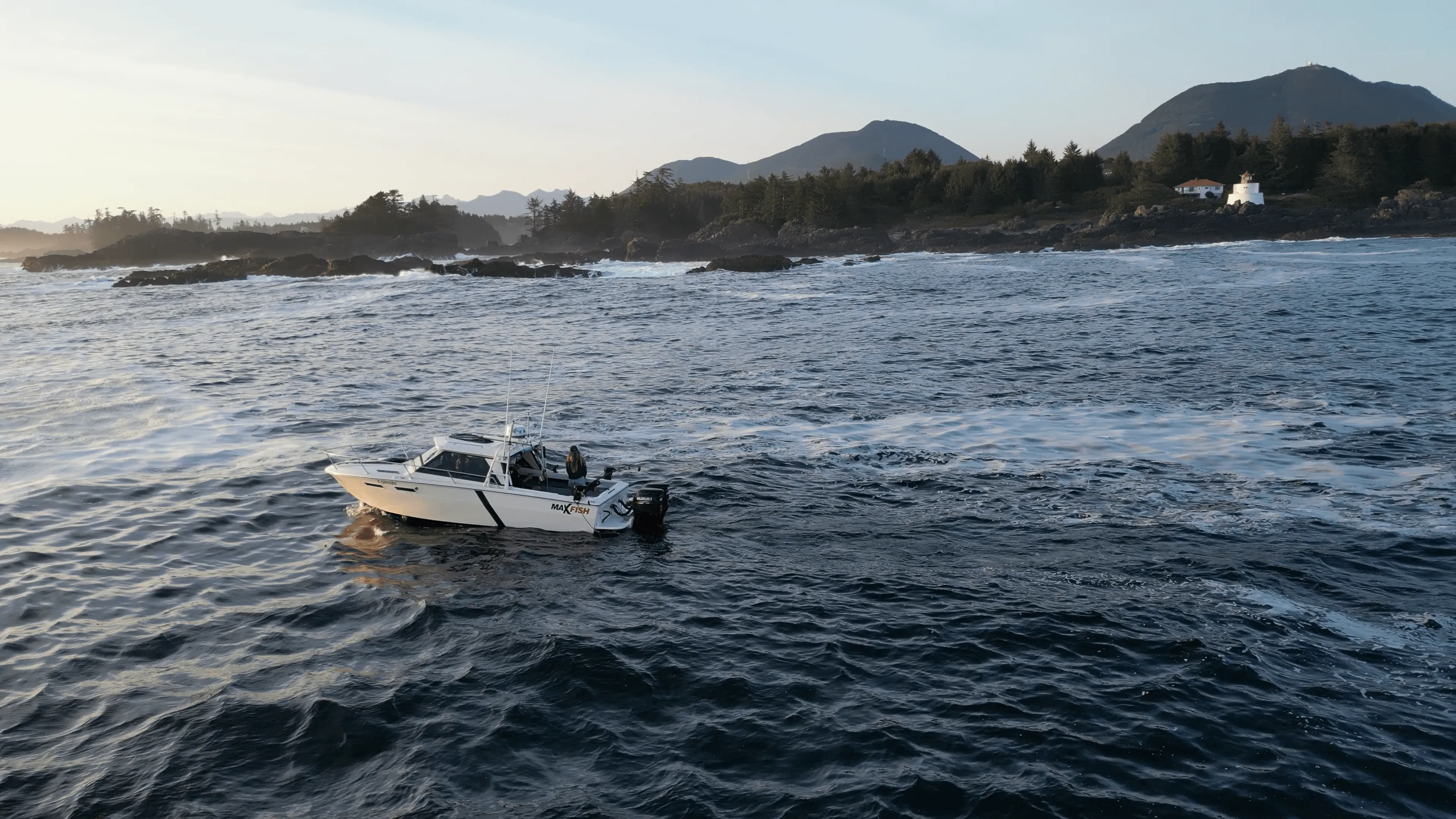 A boat navigates choppy waters near a rocky coastline, with distant mountains and soft evening light.