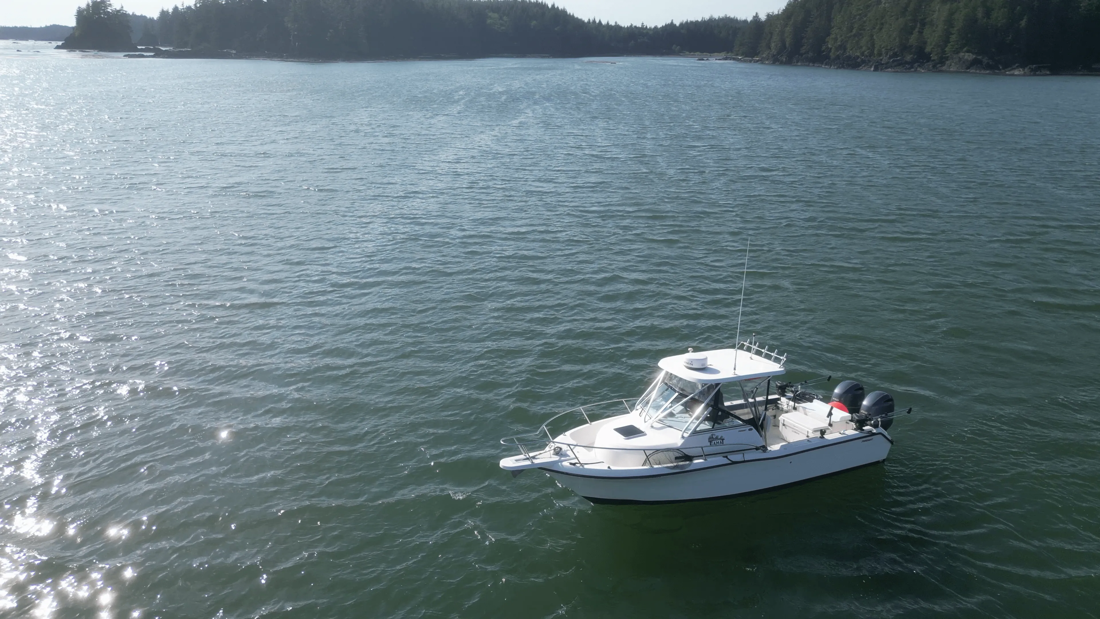 A small white boat on a tranquil lake, surrounded by wooded shores under a clear sky.