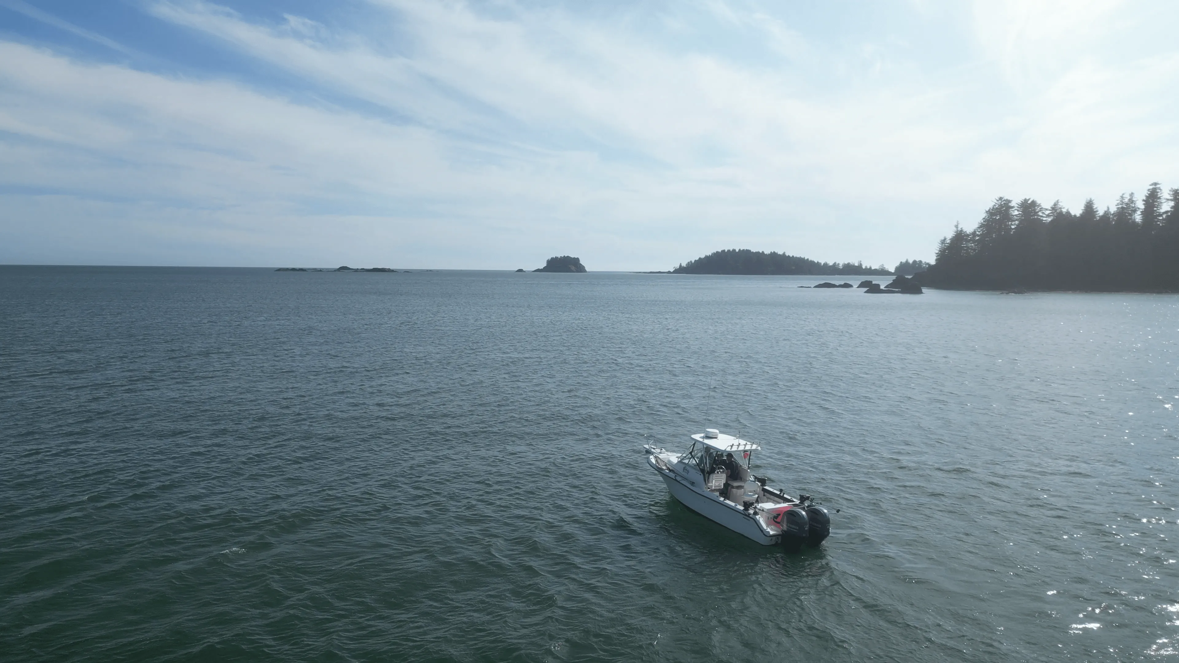 Boat gliding on a serene ocean with distant islands and a partly cloudy sky.