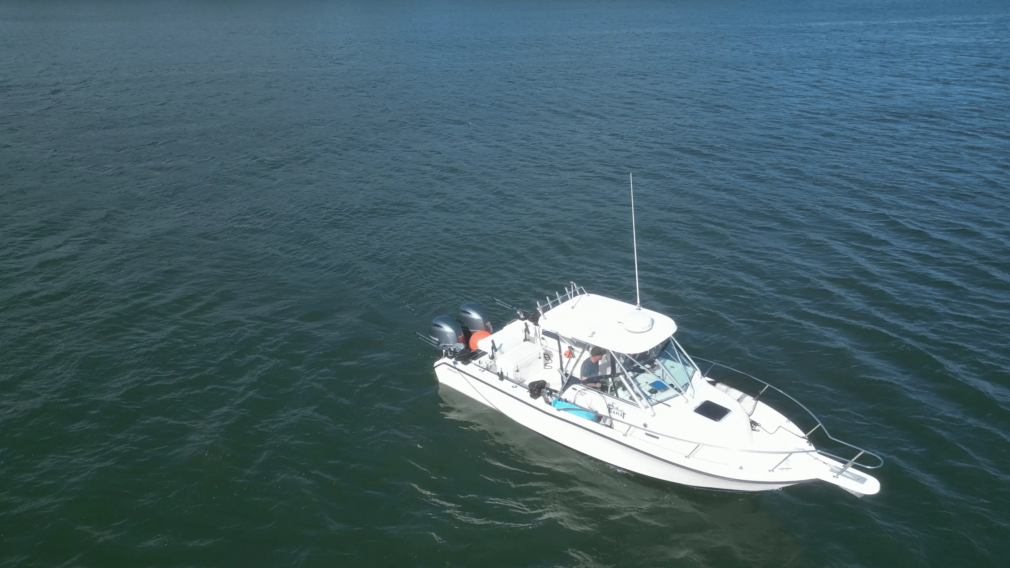 A small white boat on calm blue water, viewed from above.